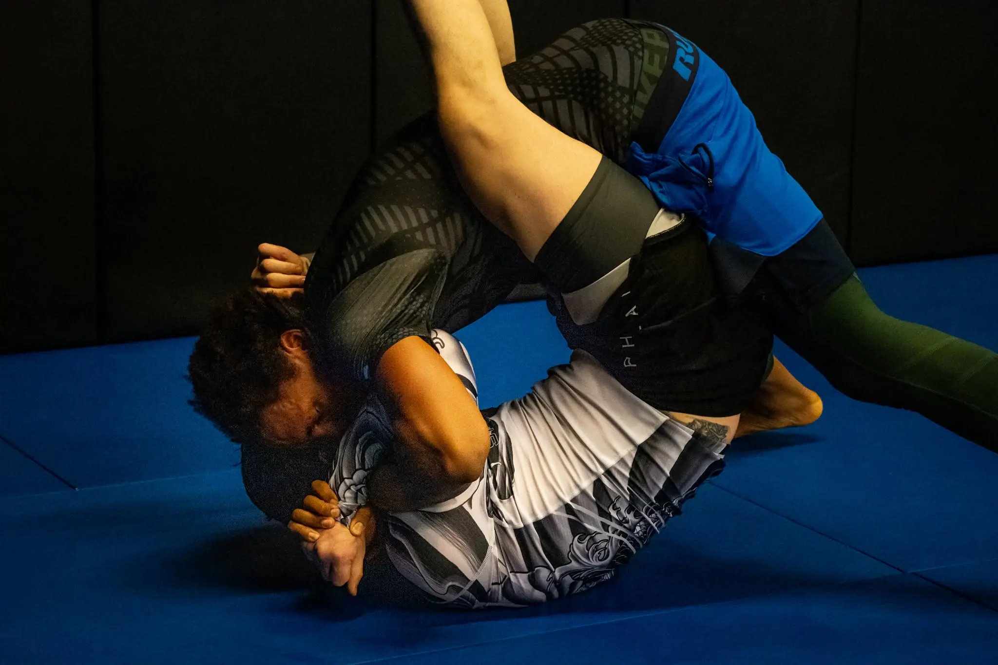 Two adults rolling no-gi at 10th Planet Portland under a head-and-arm control against the black wall