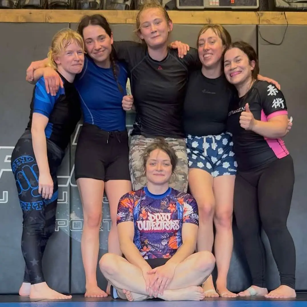 Six women in rashguards with arms around each other after a women's jiu jitsu class at 10th Planet Portland