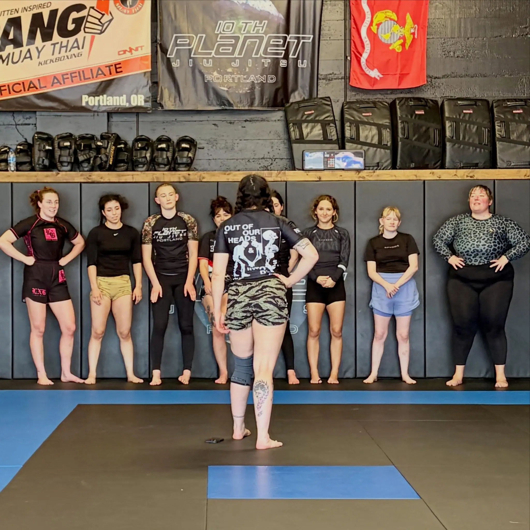 Women's jiu jitsu class at 10th Planet Portland lined up along the wall while an instructor addresses them