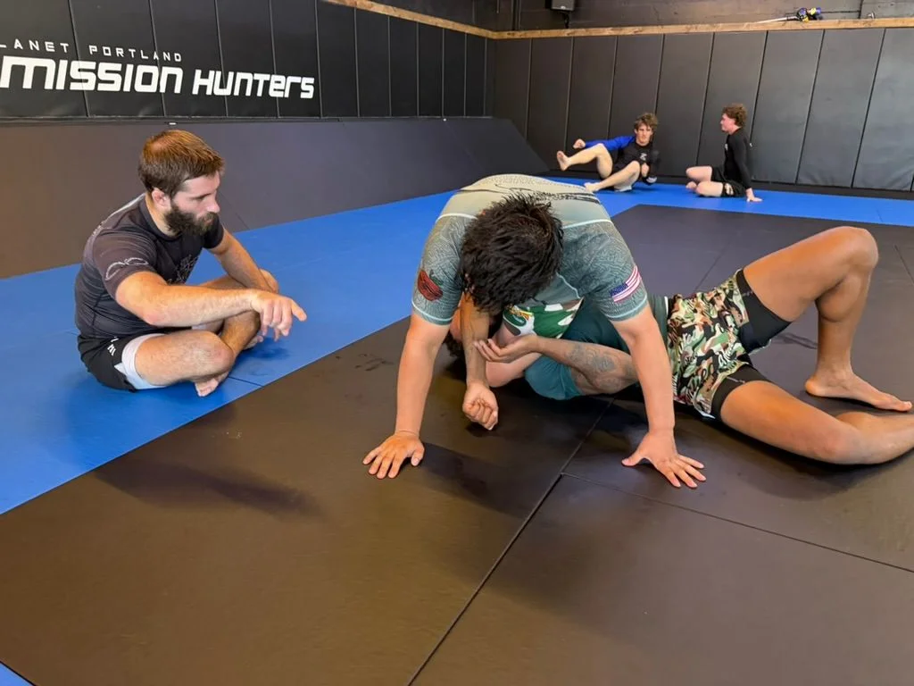 Adults drilling in pairs on the mats at 10th Planet Portland while a coach watches from the side, more pairs working in the background